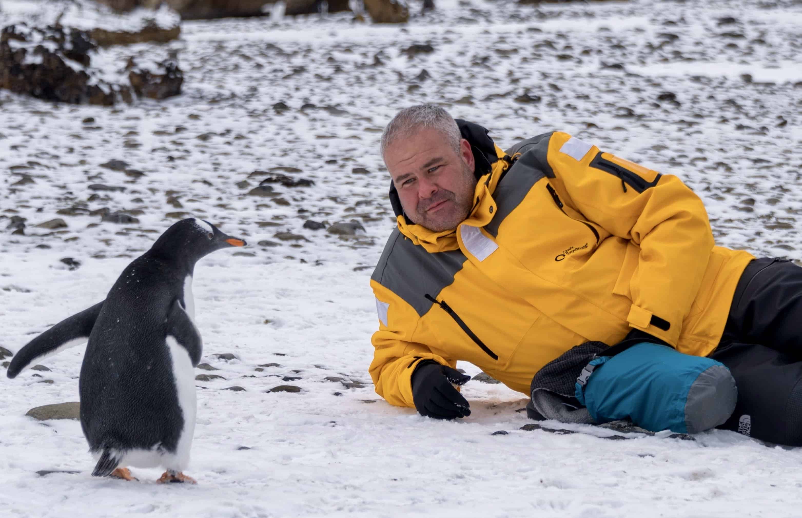 Laying on the snow covered beach of Brown Bluff, Antarctica with a penguin. Antarctica Expedition.